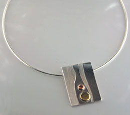 oblong silver pendant with copper and brass